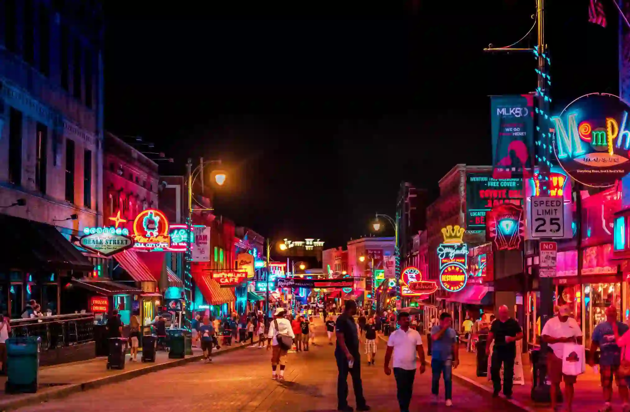 Vibrant night scene on Beale Street in Memphis, with neon signs glowing above blues clubs, bars, and live music venues, and crowds of people walking along the historic street
