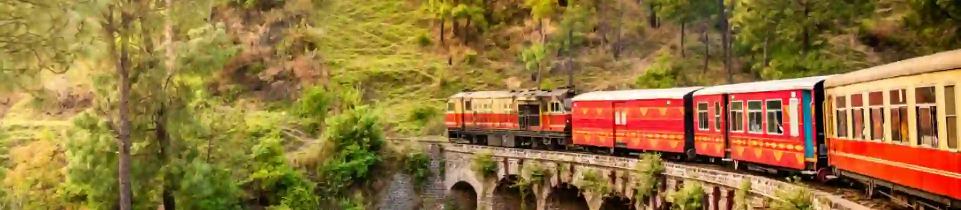 The heritage toy train crossing a railway bridge on the Kalka–Shimla route, surrounded by lush green hills and trees