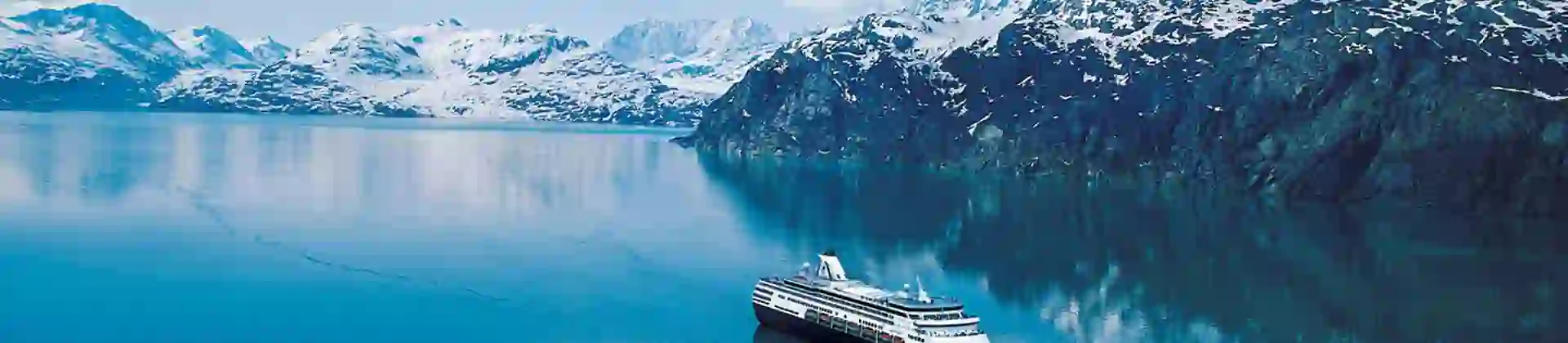 A Holland America Line cruise ship sailing through the clear blue waters of the Inside Passage near Alaska, with snow-capped mountains in the distance