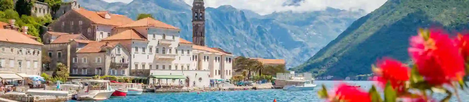 Scenic panorama view of the historic town of Perast at famous Bay of Kotor with blooming flowers on a beautiful sunny day with blue sky and clouds in summer, Montenegro, southern Europe