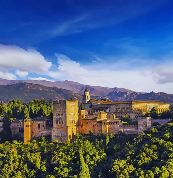 Panoramic view of the Alhambra Palace in Spain on a sunny day, with its historic architecture set against a backdrop of rolling hills and a bright blue sky