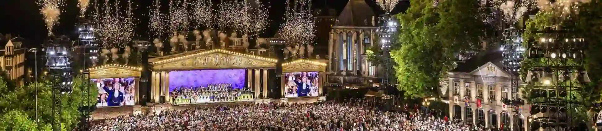 André Rieu performing in Maastricht’s Vrijthof Square, with his orchestra on stage and colourful fireworks lighting up the night sky