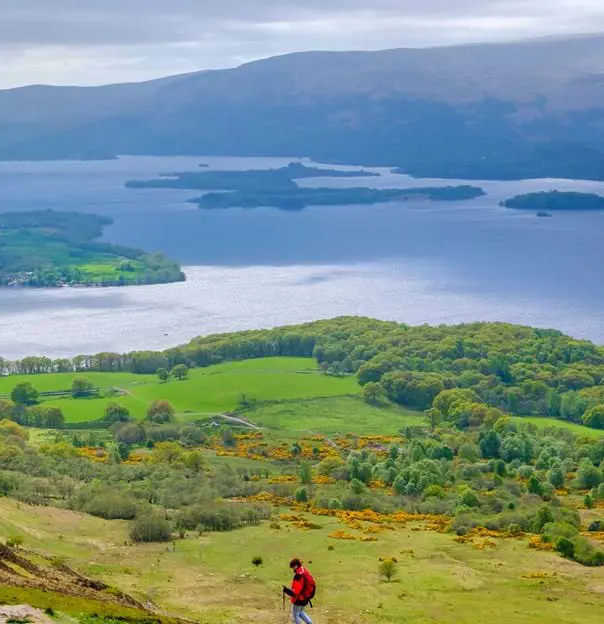 High angle view of Loch Lomond and Trossachs National Park, with a man wearing a red jacket walking down the mountain
