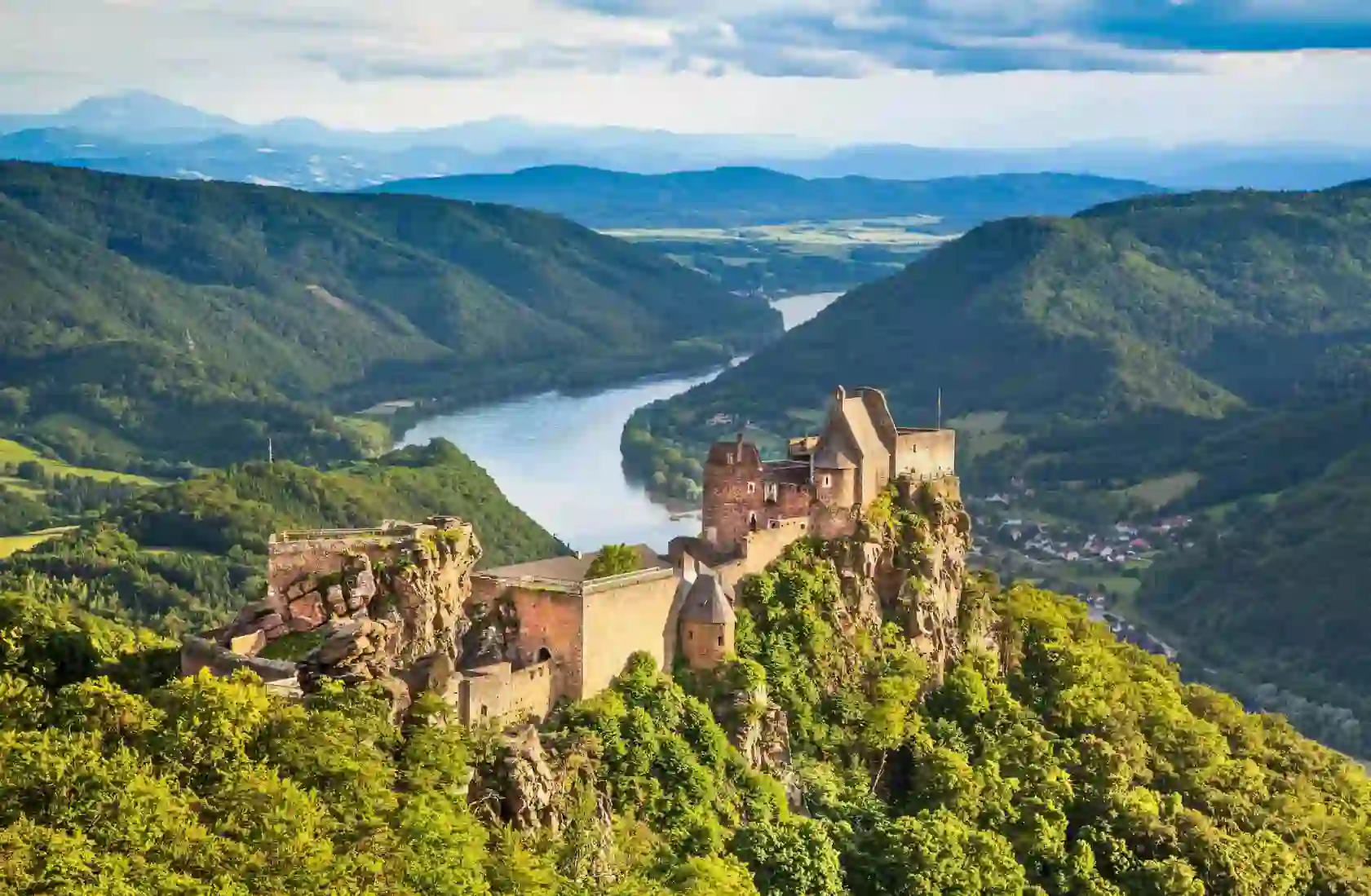 Ruins of a medieval castle perched on a rocky hilltop overlooking the Danube River in the Wachau Valley, Austria, surrounded by lush green hills and distant mountains