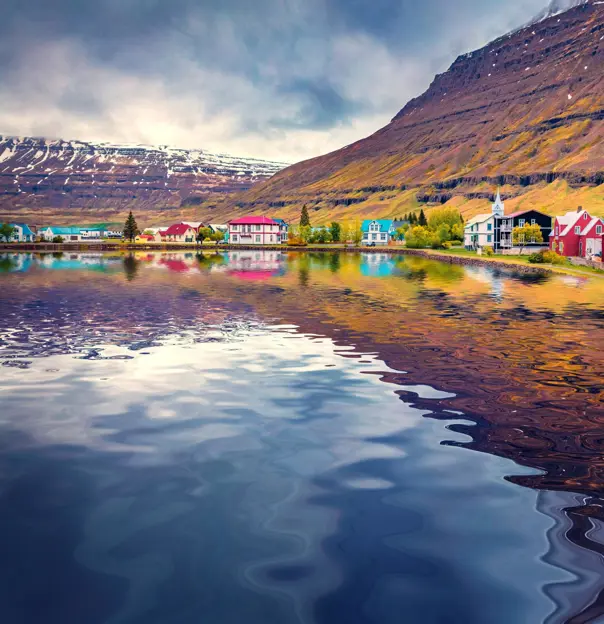 Seydisfjordur small town reflected in the caslm waters of Atlantic ocean. Dramatic summer scene of east west Iceland, Europe. Traveling concept background.