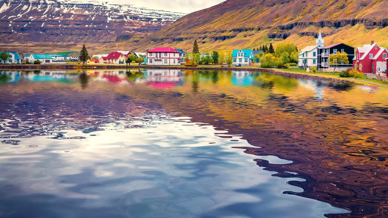 Seydisfjordur small town reflected in the caslm waters of Atlantic ocean. Dramatic summer scene of east west Iceland, Europe. Traveling concept background.