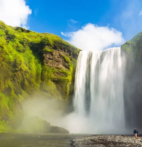 Waterfall surrounded by mossy rock. Steam coming off the water, people stood below the waterfall.