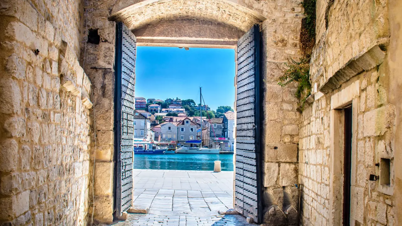 View of a boat on some water, with buildings behind it, through open doors in a stone walkway. A bright blue sky.