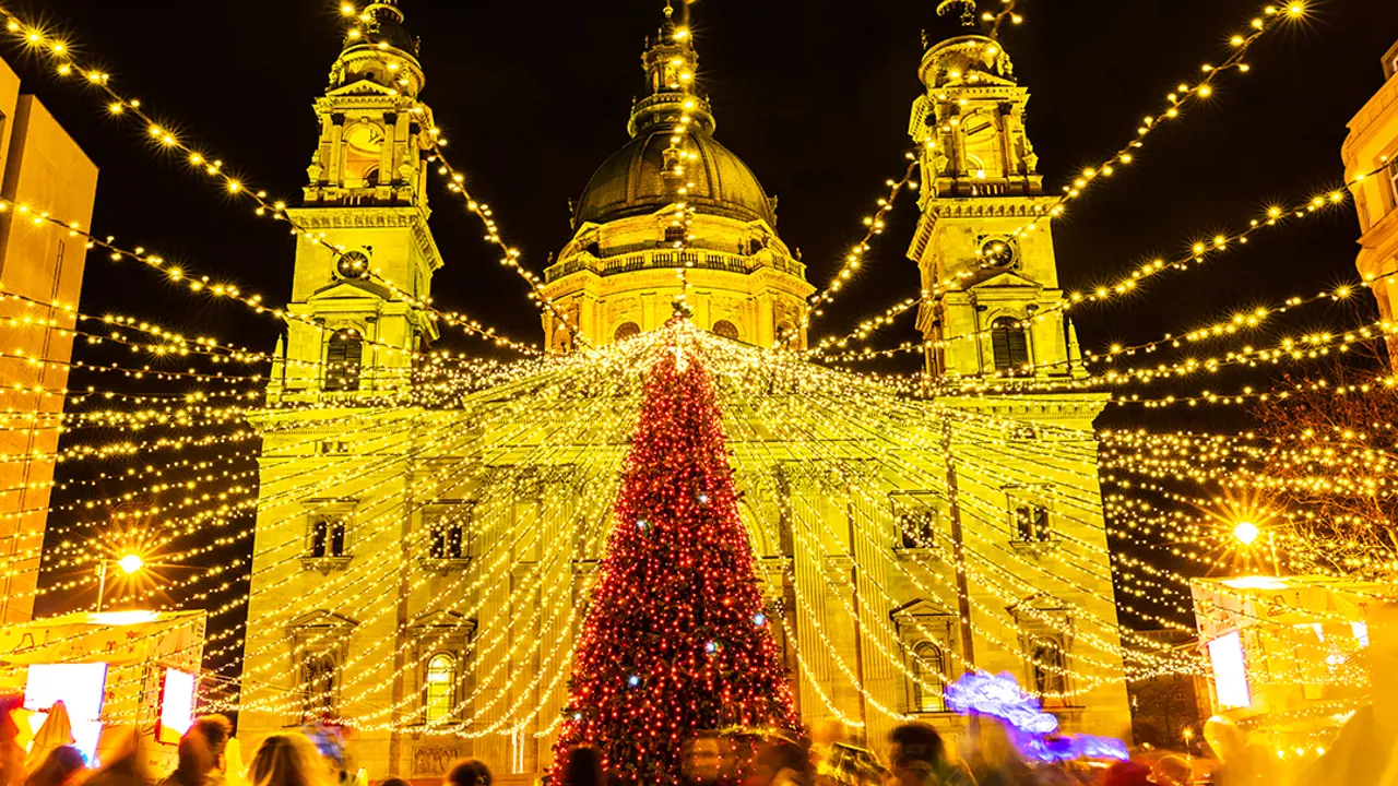 Low angle shot of a large christmas tree covered in red lights, with gold fairy lights strung out of it. Lit up St. Stephen's Basilica behind it.