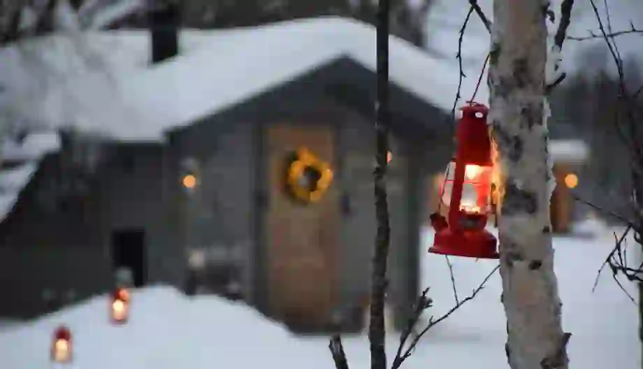 Close up of a lantern tied to a tree with Santa's Grotto in the background, in the snowy woods