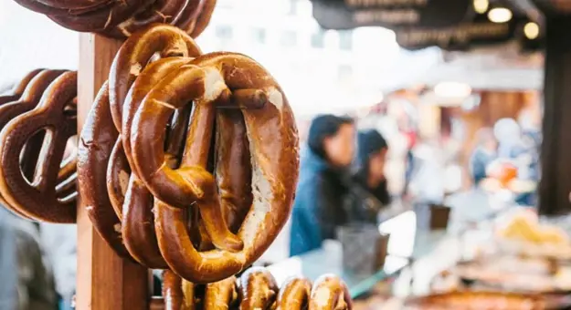 Pretzels hanging on a wooden peg, with blurry people in the background