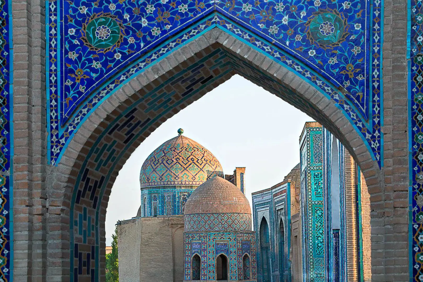 A tiled archway in Samarkand, Uzbekistan, framing a view of two domed temple roo