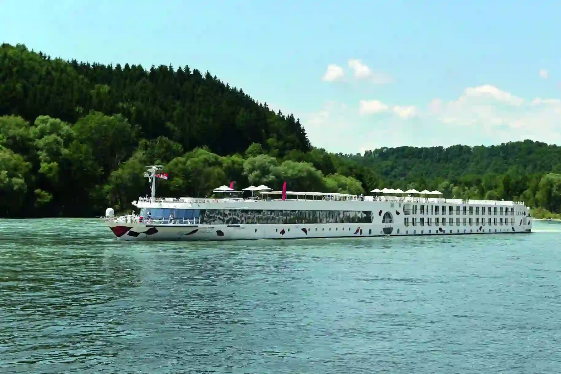 An A-ROSA river cruise ship sailing down a river with trees in the background