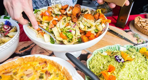 Close up of a variety of dishes, a hand serving a salad