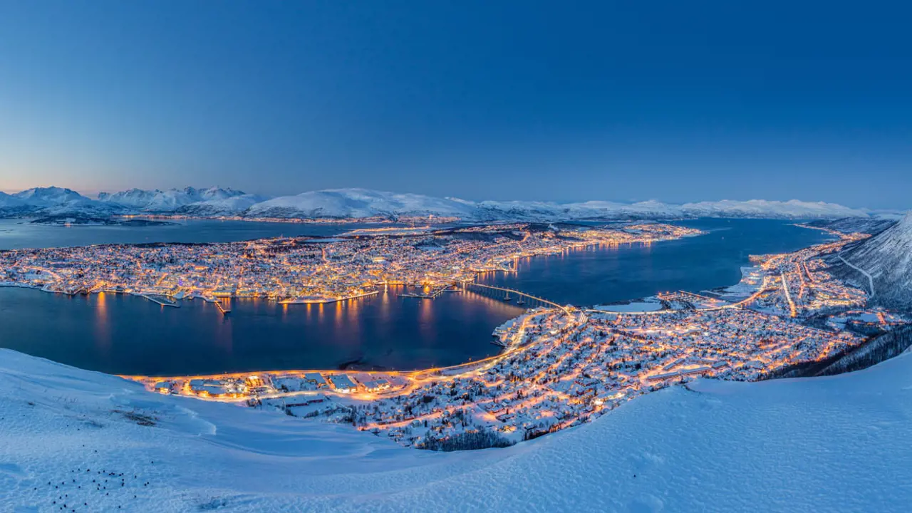 View of Tromso in the snow, at night time with light from the buildings lighting up the town