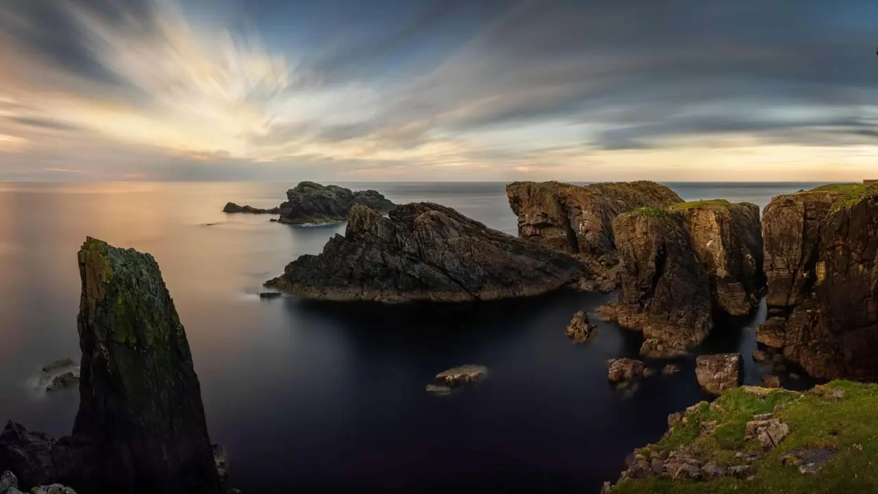 Long shot of the coast of the Isle of Lewis at sunset, showing the Butt of Lewis Lighthouse on the far right, looking out to sea