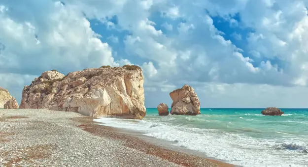 A cloudy day with waves crashing on a pebbled beach near Aphrodite’s Rock in Cyprus