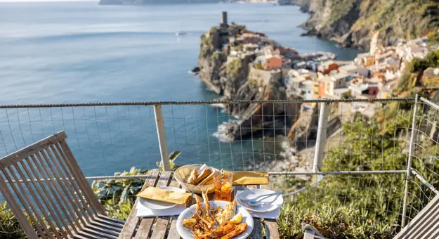 Table of food on a balcony with the view of the sea and the town of Clinque Terre