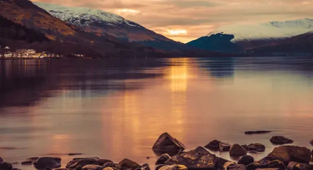 Loch Lomond at sunset, with snowy mountains in the distance