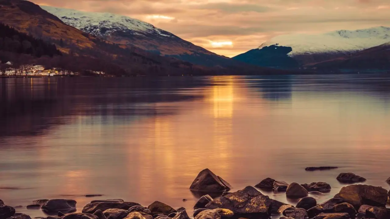 Loch Lomond at sunset, with snowy mountains in the distance