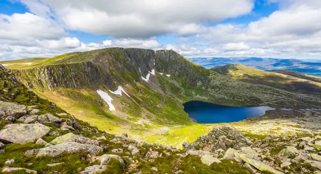 View of Cairngorms National Park, with a small body of water in the centre and a cloudy, but blue sky