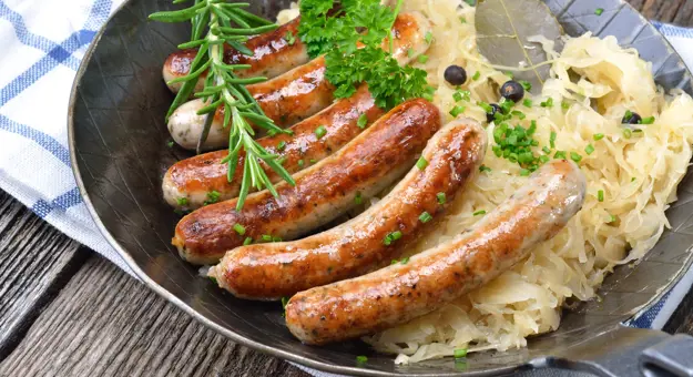 Plate of traditional German bratwurst and sauerkraut on a white and blue checkered cloth.