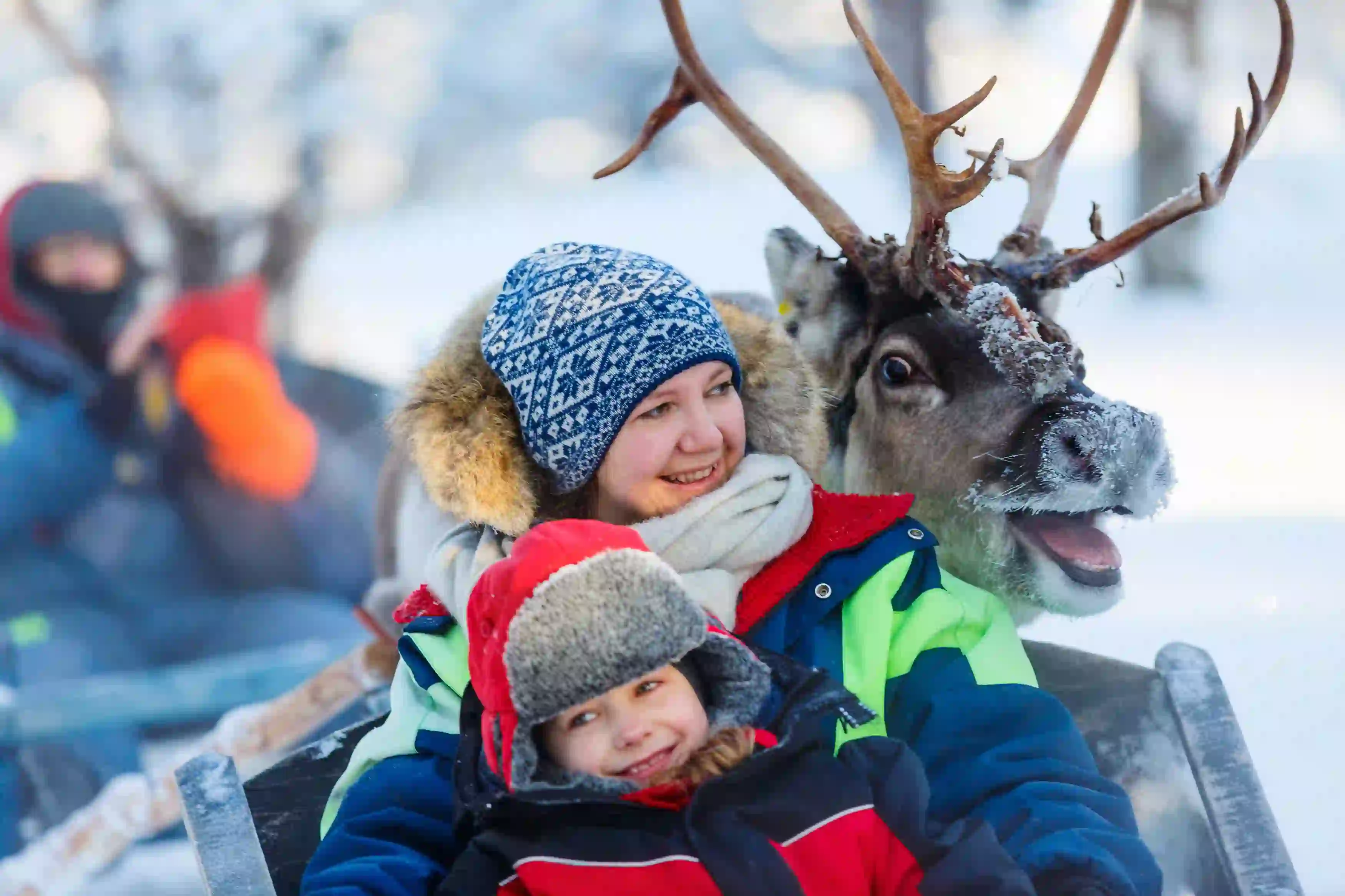 Mother and child sat with a reindeer, smiling 