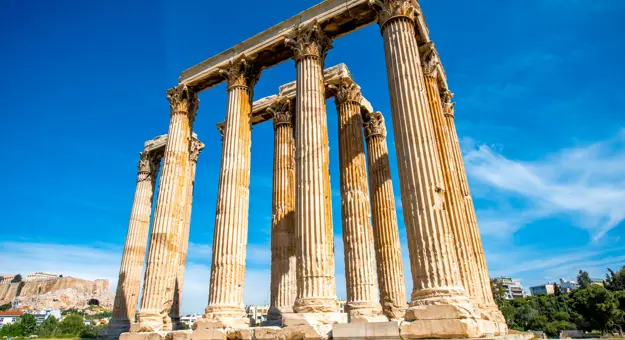 Low angle shot of temple ruins, with pillars. Blue sky behind