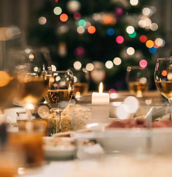 Close up of a laid dinner table, with glasses of white wine and bowls of food, with a blurry background of fairy lights