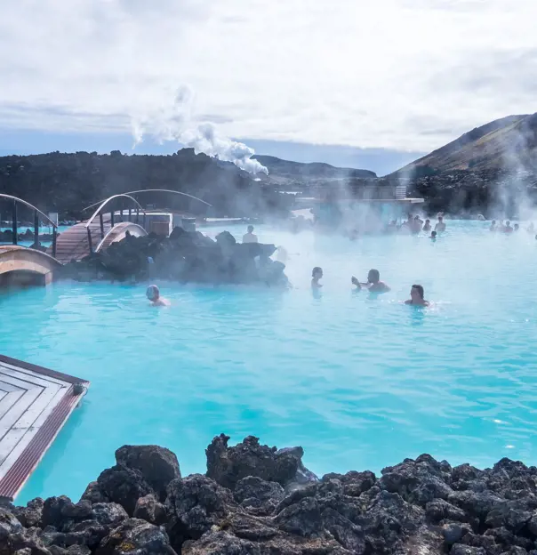 Geothermal lagoon in Iceland - bright blue water with steam coming off, surrounded by black rock. People swimming.