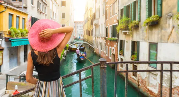 Back of a lady looking over a canal in Venice, with a gondola travelling down it and buildings either side