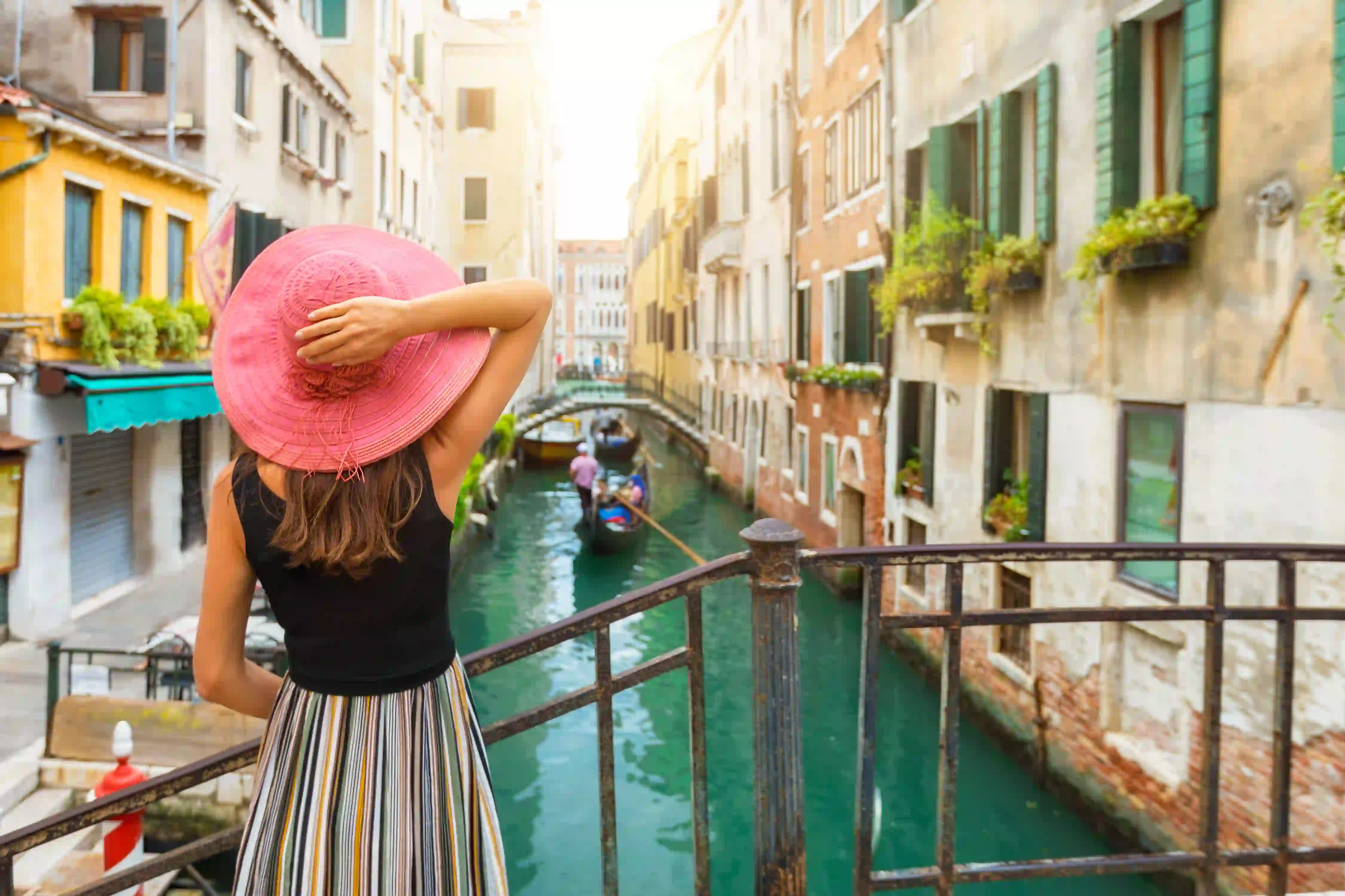 Back of a lady looking over a canal in Venice, with a gondola travelling down it and buildings either side