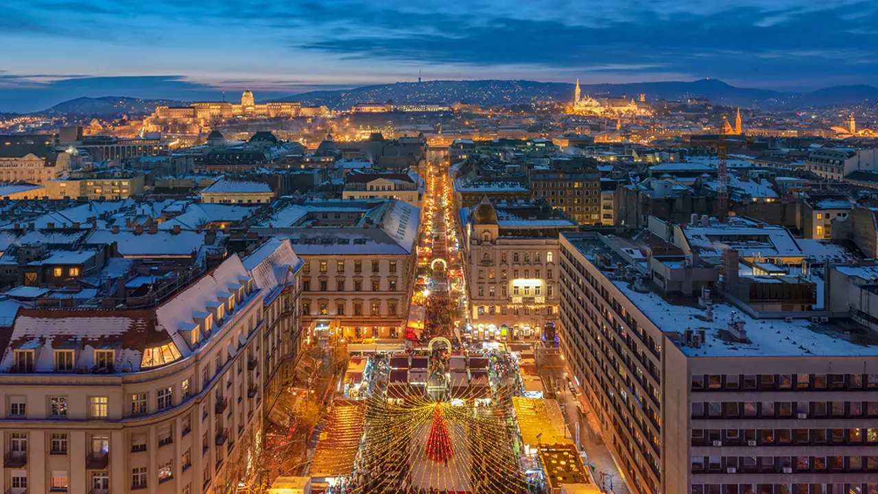 High angle shot of long street, full of people and stalls. Leading down to the forefront of the image, to the busy square with a red Christmas tree in the centre, with gold lights trailing out of it.