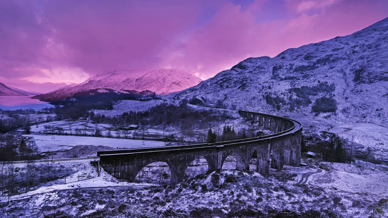 Glenfinnan Viaduct in the snow, surrounded by mountains and a purple sky