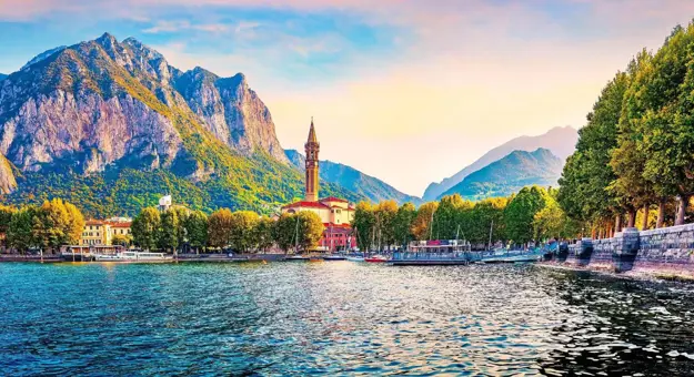 A view of Lake Como with a small church tower and mountains and trees in the background