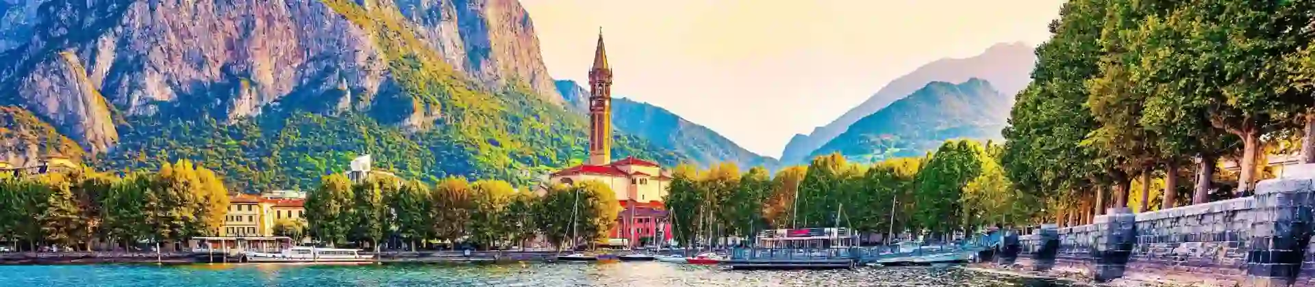 A view of Lake Como with a small church tower and mountains and trees in the background