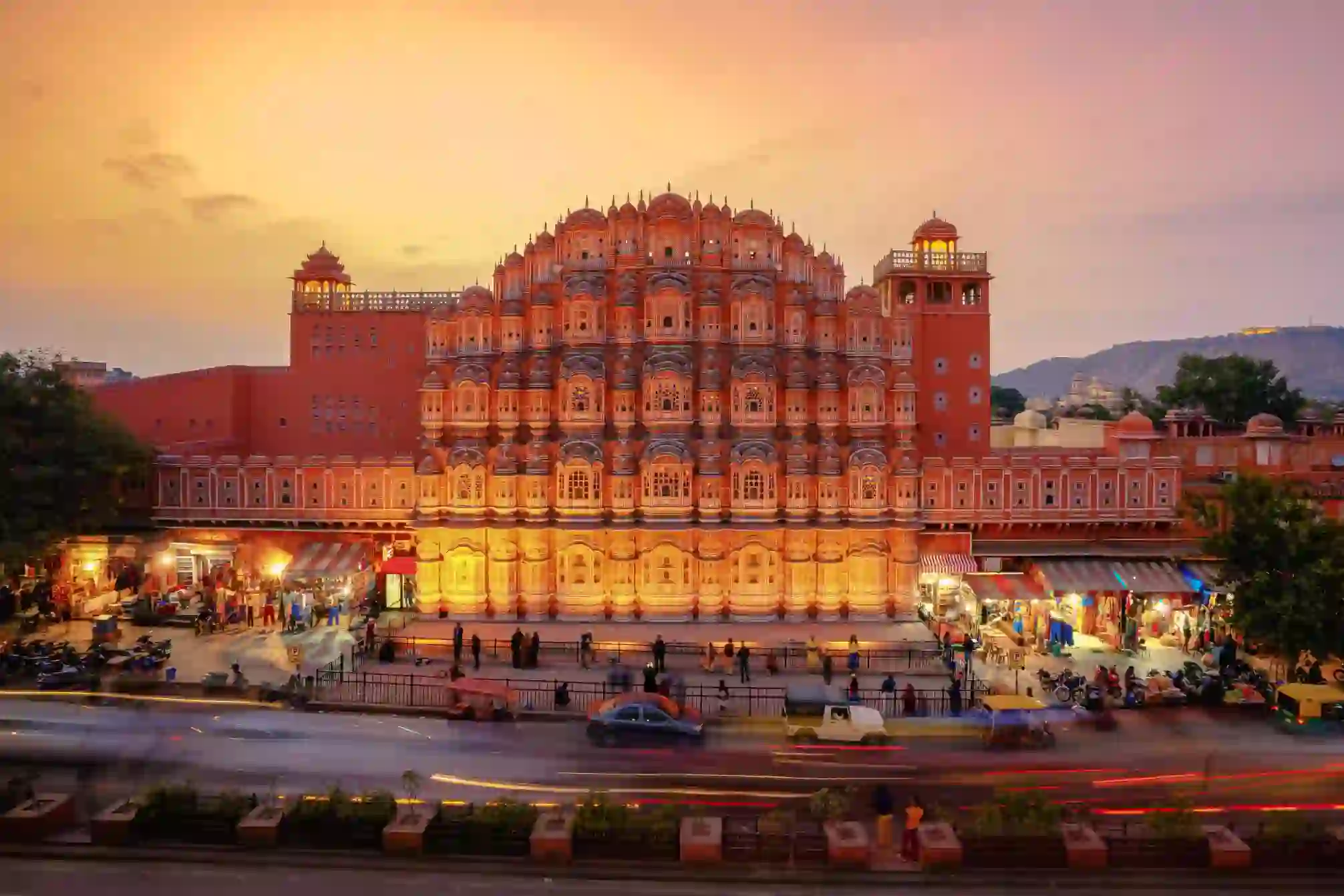 The Palace of the Winds in Jaipur illuminated at sunset, its ornate pink façade overlooking the street below