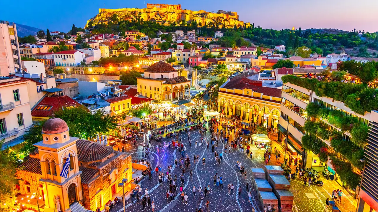 High angle view of a town in the evening, with lit up buildings. A rocky hill with ruins on the top.