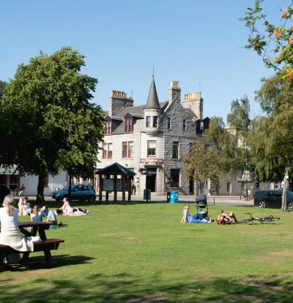 People enjoying sunny day and lying in the grass outside of the Glenmuick Church in the town centre of Ballater. Balmoral bar in the background.