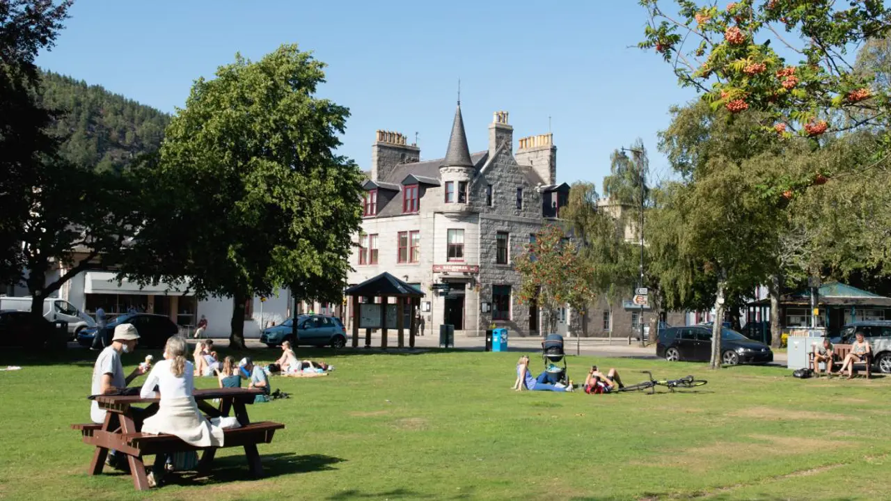 People enjoying sunny day and lying in the grass outside of the Glenmuick Church in the town centre of Ballater. Balmoral bar in the background.