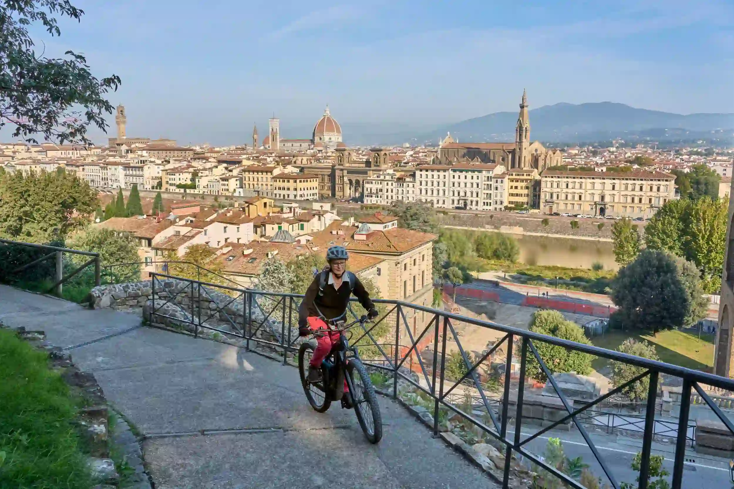 Woman cycling along a pathway on a mountain in Florence, with a view of the city