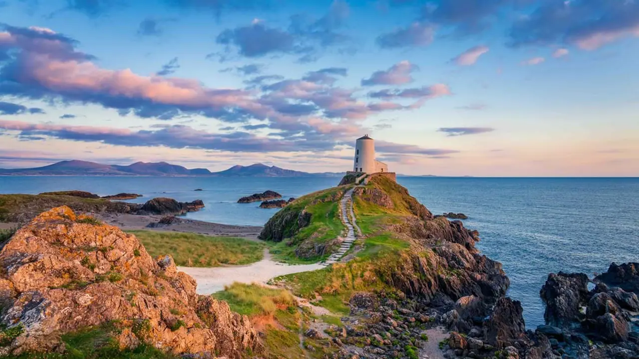 Long-shot of Twr Mawr Lighthouse on the top of a hill looking out to sea at sunset