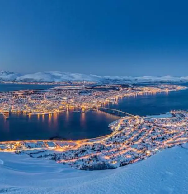 View of Tromso in the snow, at night time with light from the buildings lighting up the town