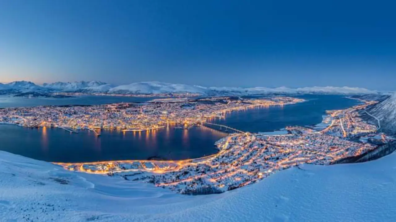 View of Tromso in the snow, at night time with light from the buildings lighting up the town