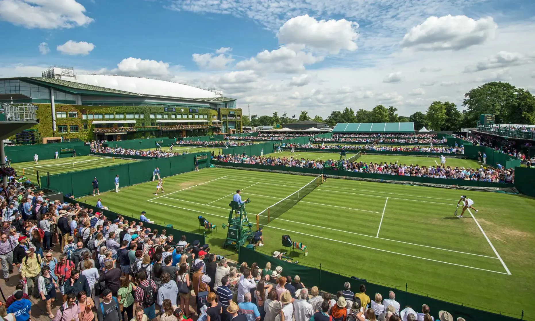 Crowds watching tennis matches on the grass courts at Wimbledon under a blue sky