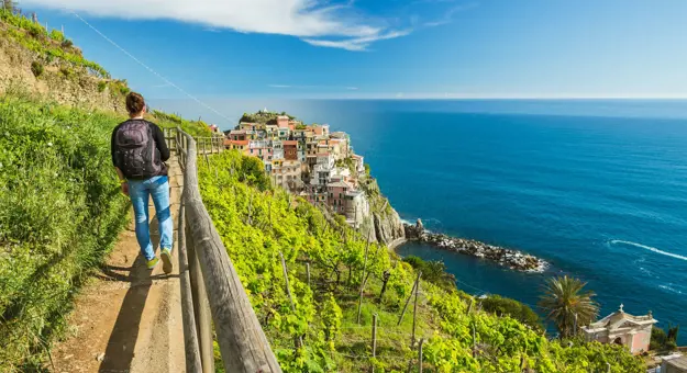 Back of a man hiking in Clinque Terre, on the side of a mountain by the sea