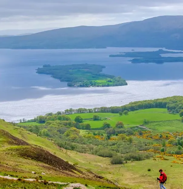 High angle view of Loch Lomond and Trossachs National Park, with a man wearing a red jacket walking down the mountain