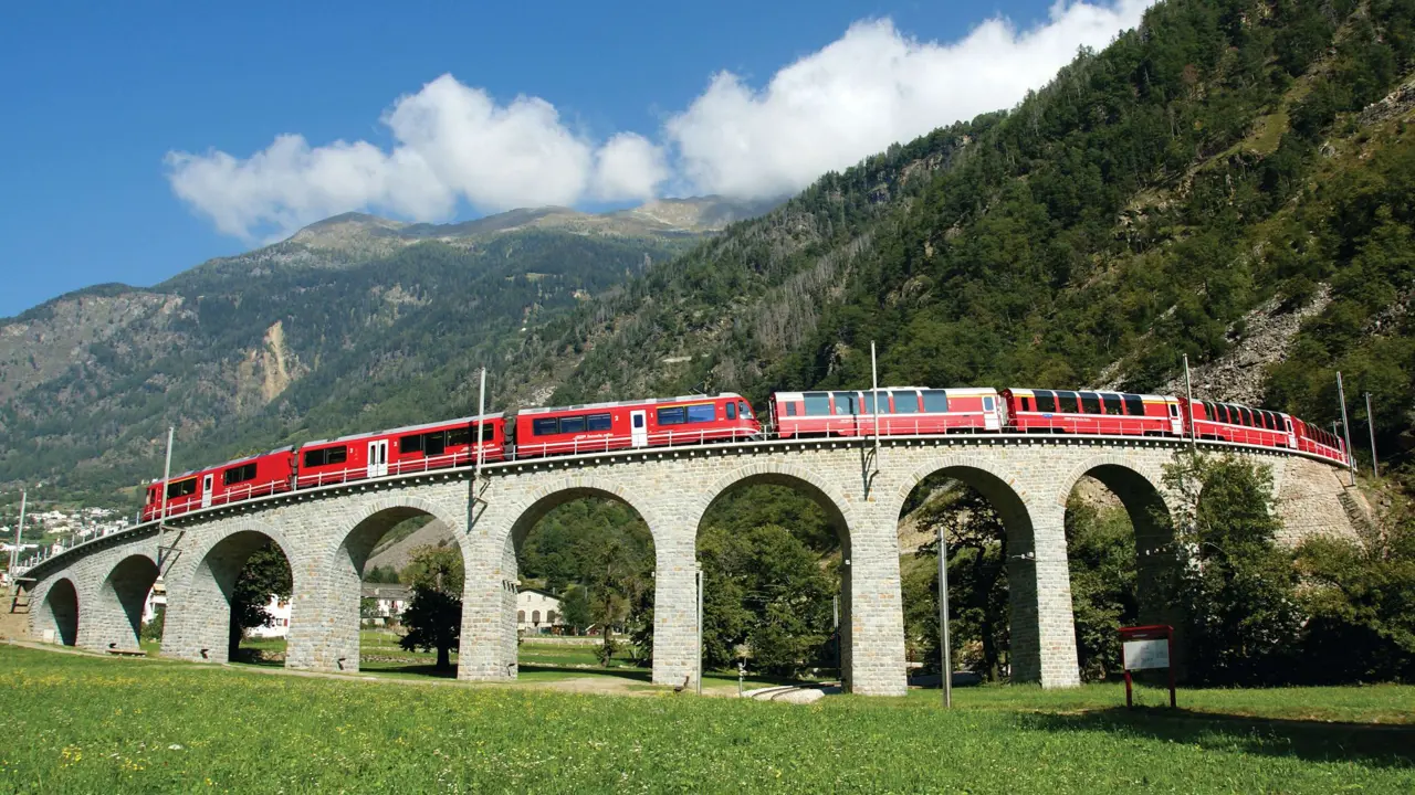 The Bernina Express going across a bridge, with grassy mountains in the background