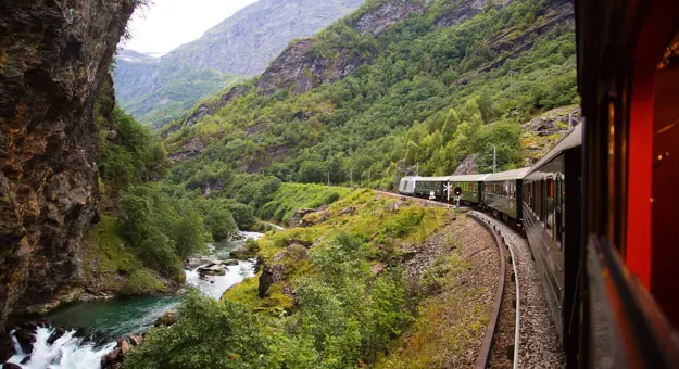 Train going through the mountains by a small stream of water