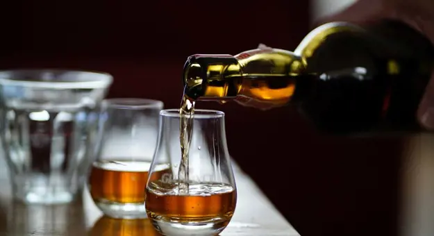 Close up of a glass of Scottish whisky being poured with dark lighting